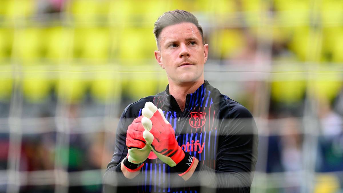 Piłkarz Marc-Andre ter Stegen w stroju bramkarskim FC Barcelony, w rękawicach bramkarskich, na tle trybun stadionu.