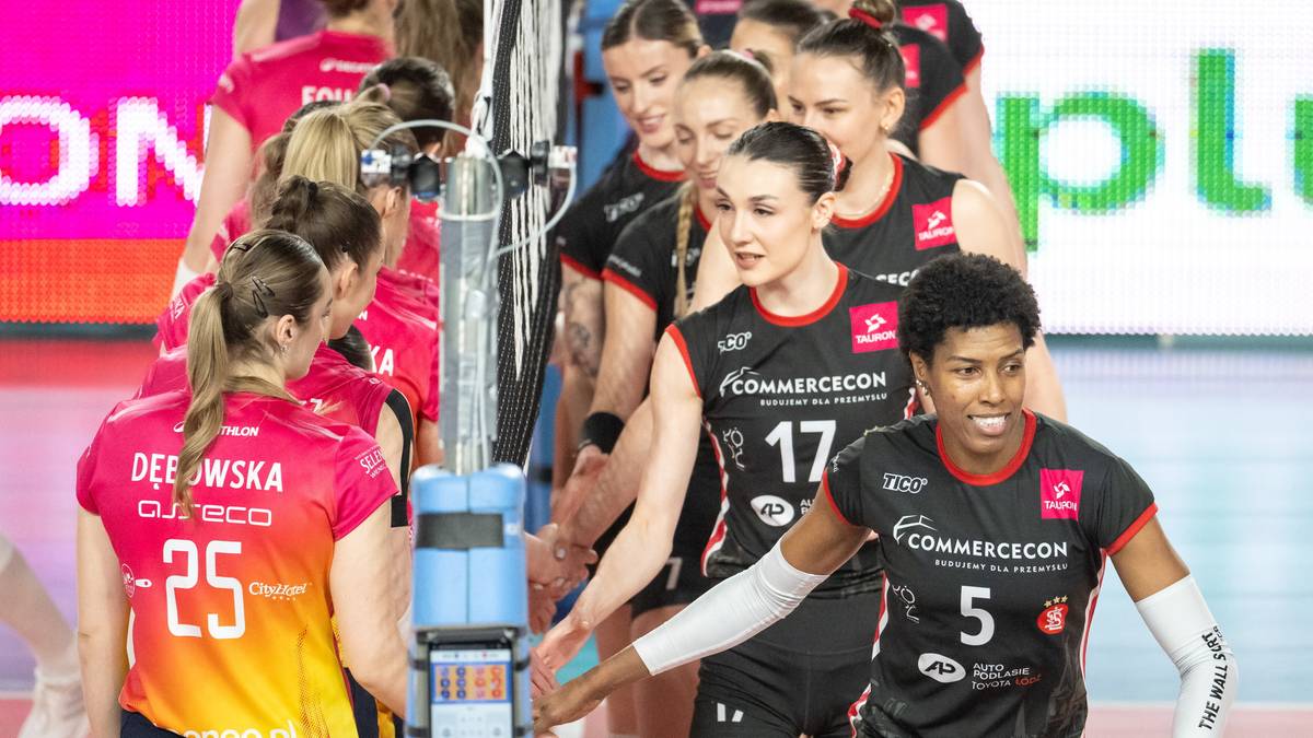Siatkarki w czarnych strojach z numerami na plecach i czerwonymi wstawkami stoją w szeregu i witają się po meczu.