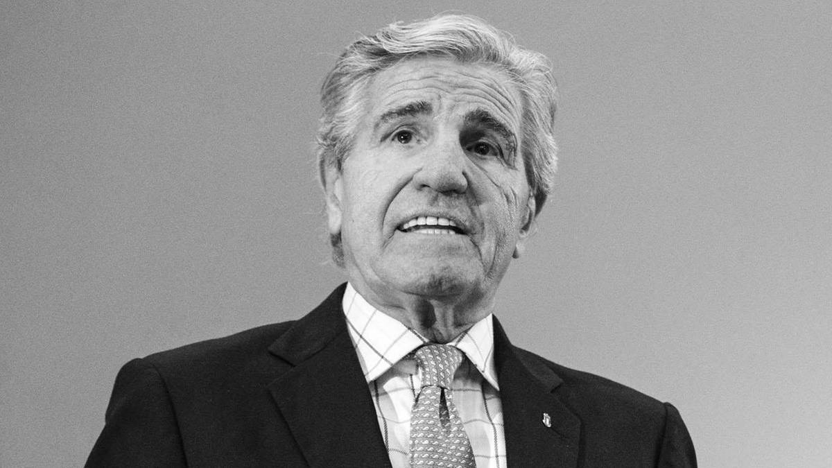 Portret czarno-biały starszego mężczyzny w garniturze i krawacie, patrzącego prosto w obiektyw z lekko otwartymi ustami.