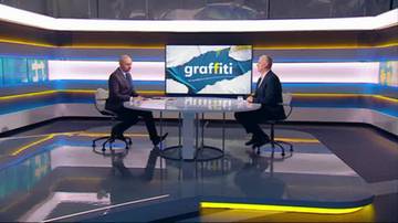 Dw&oacute;ch mężczyzn siedzi naprzeciwko siebie przy okrągłym stole w studiu telewizyjnym. Na dużym ekranie w tle widnieje logo programu "graffiti".