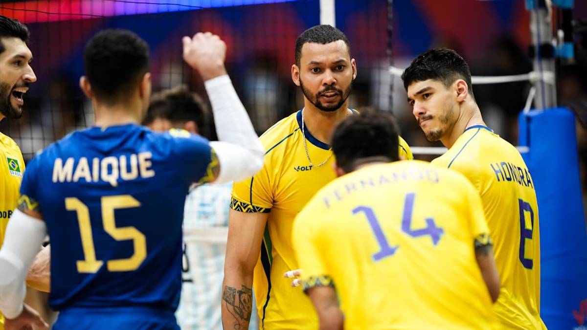 Grupa siatkarzy w żółtych koszulkach stoi na boisku. Dwóch siatkarzy rozmawia ze sobą.