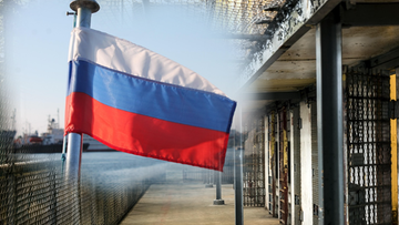 Flaga Rosji powiewająca na wietrze nad nabrzeżem, obok widoczne cele więzienne.