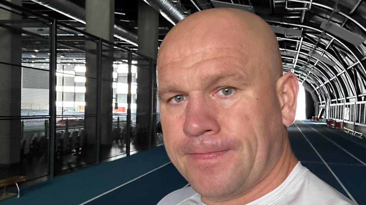 Łukasz R&oacute;żański w białej koszulce z logo LOTTO, z płotkami lekkoatletycznymi w tle.