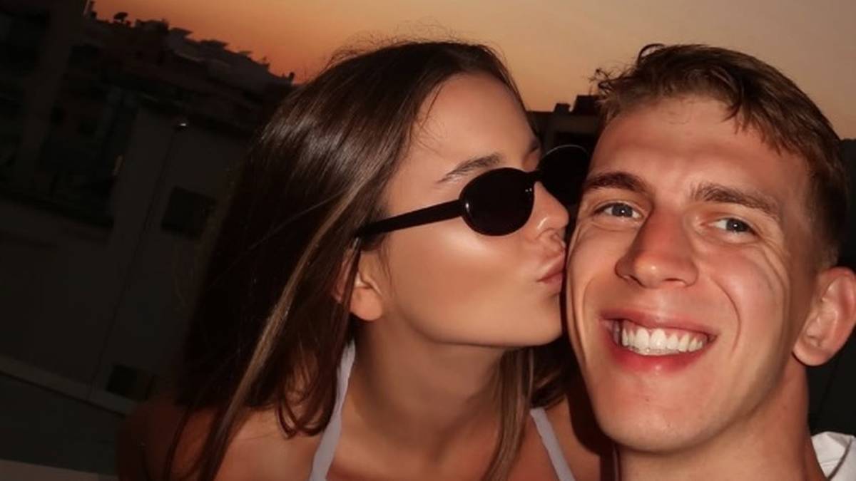 Młoda kobieta w okularach przeciwsłonecznych całuje w policzek uśmiechniętego mężczyznę.