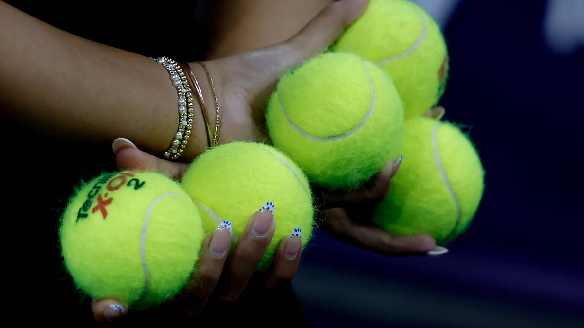 Dłoń kobiety trzymająca pięć piłek tenisowych.