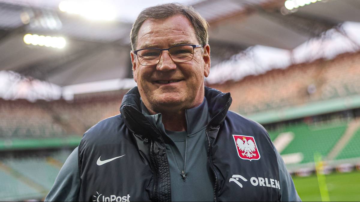 Michał Urban, trener reprezentacji Polski, w kamizelce z godłem Polski na tle stadionu.