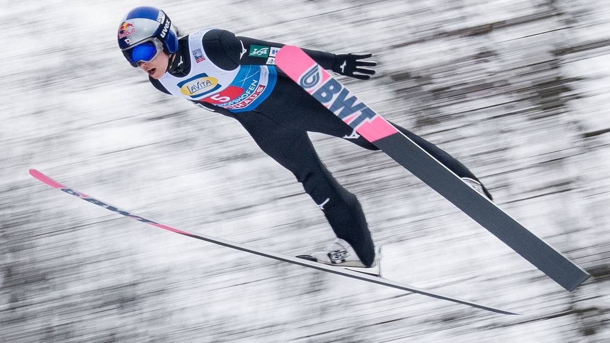 Skoczek narciarski w powietrzu podczas zawod&oacute;w, na nartach i w kombinezonie.