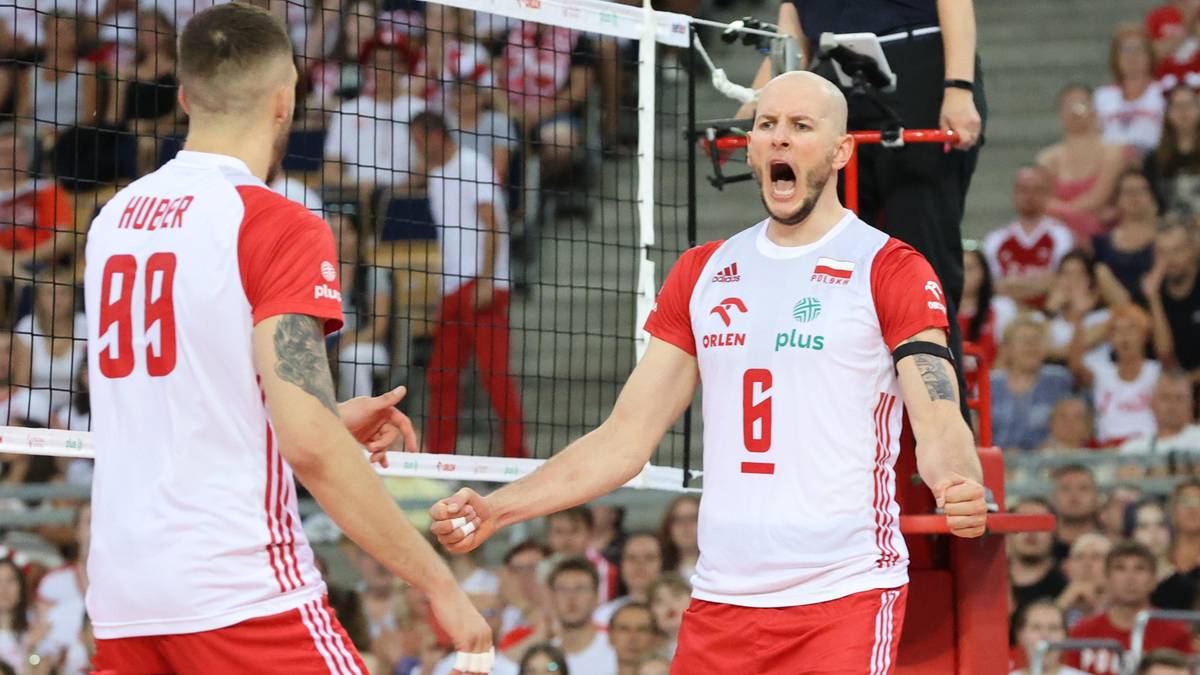 Dwóch siatkarzy w białych koszulkach z czerwonymi akcentami świętuje zwycięstwo, jeden z nich krzyczy z radości.