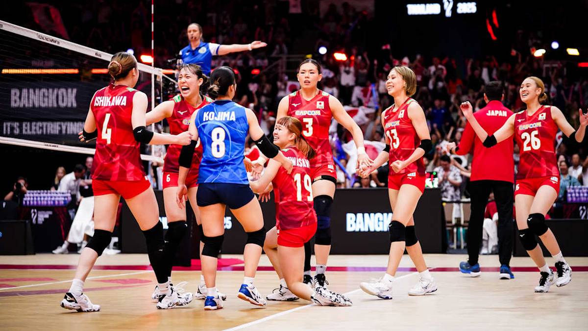 Grupa zawodniczek w czerwonych koszulkach świętuje na boisku do siatkówki, niektóre zawodniczki trzymają się za ręce lub podnoszą je do góry w geście radości. Na boisku widać siatkę i bandy reklamowe.