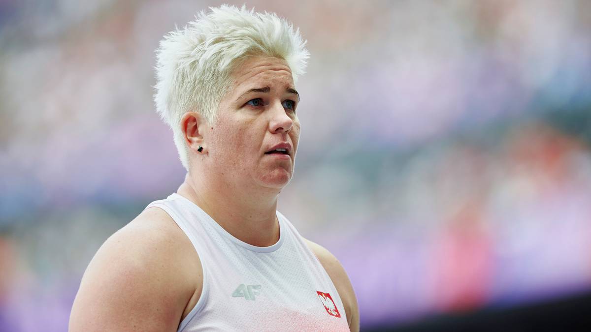 Portret Anity Włodarczyk, polskiej lekkoatletki, mistrzyni olimpijskiej w rzucie młotem. Jest na niej skupiona, z kr&oacute;tkimi blond włosami, w białej koszulce sportowej.