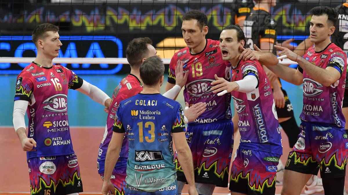 Grupa siatkarzy w kolorowych strojach sportowych stojących blisko siebie na boisku, w tle trybuny.