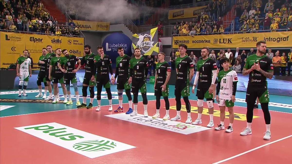 Drużyna siatkarska w zielonych strojach stoi na parkiecie hali sportowej.