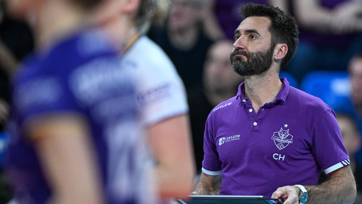 Trener siatk&oacute;wki w fioletowej koszulce obserwuje mecz, trzymając tablet.