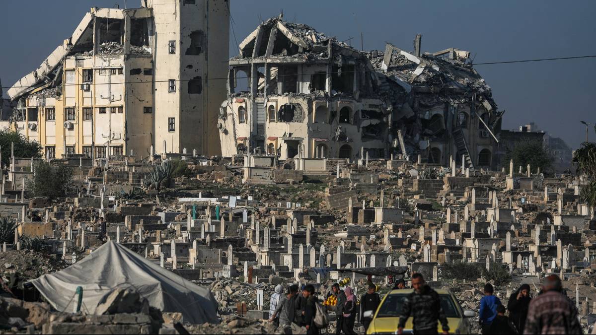 Grupa ludzi w pobliżu zniszczonych budynków i cmentarza.