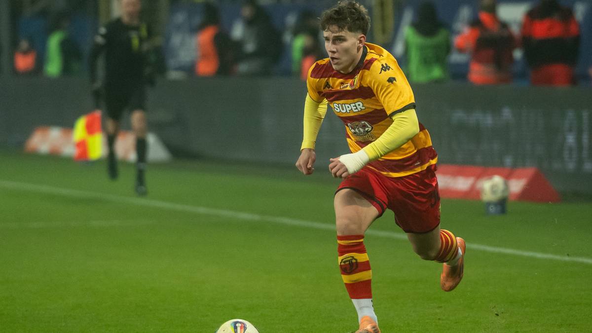 Piłkarz Oskar Pietuszewski w koszulce Jagiellonii Białystok prowadzi piłkę na boisku.