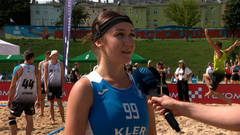Młoda kobieta w niebieskim stroju sportowym z numerem 99 na piersi udziela wywiadu na plaży.