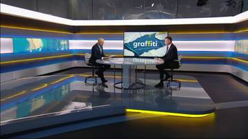 Dw&oacute;ch mężczyzn w garniturach siedzi przy okrągłym stole w studiu telewizyjnym.