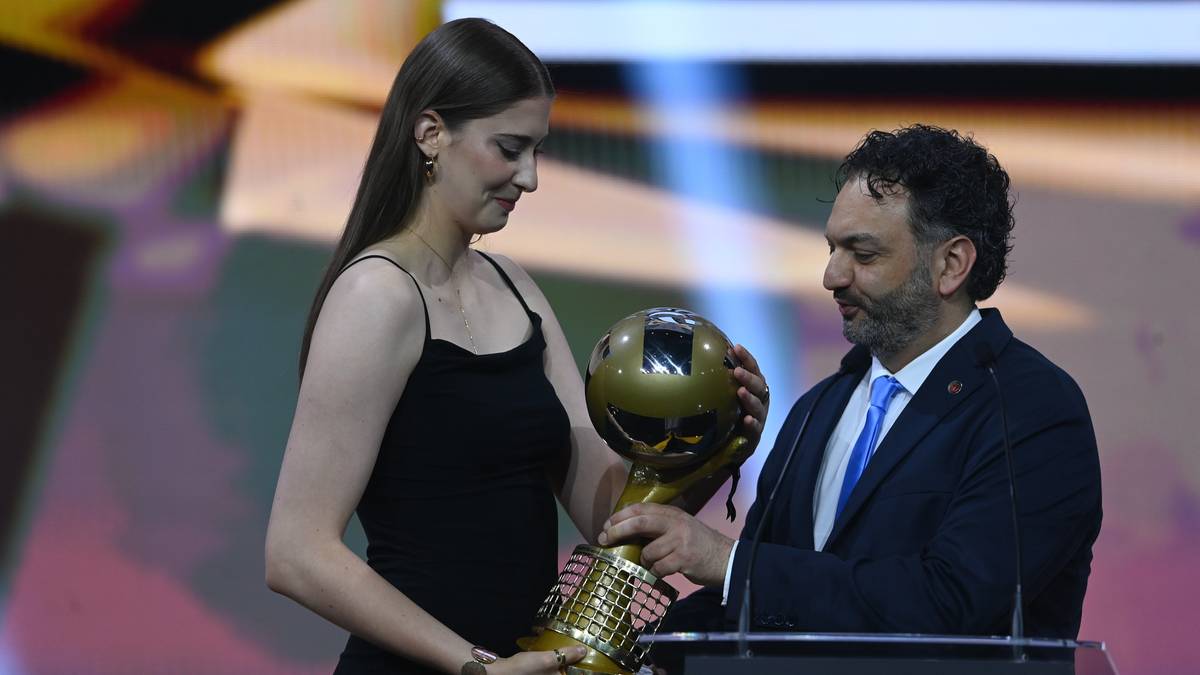 Młoda kobieta w czarnej sukience odbiera złotą statuetkę od uśmiechniętego mężczyzny w garniturze i niebieskiej koszuli.