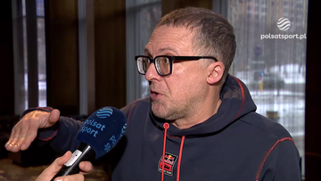 Tomasz Lorek w okularach i ciemnej bluzie z logo Polsat Sport udziela wywiadu, trzymając mikrofon.