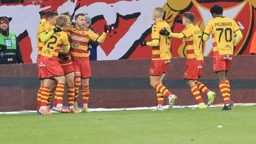 Piłkarze Jagiellonii Białystok w żółto-czerwonych strojach świętują razem na boisku.