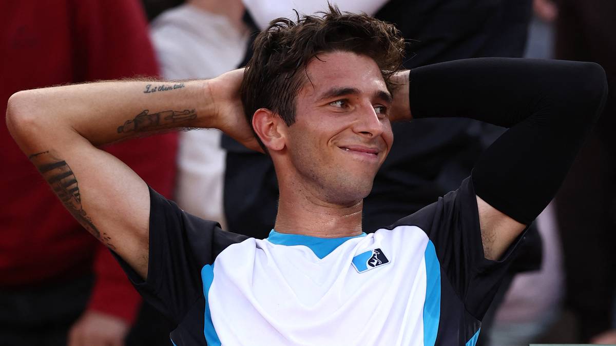 Uśmiechnięty tenisista z rękami założonymi za głowę podczas meczu.