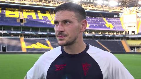 Portret mężczyzny w koszulce sportowej na tle stadionu piłkarskiego.