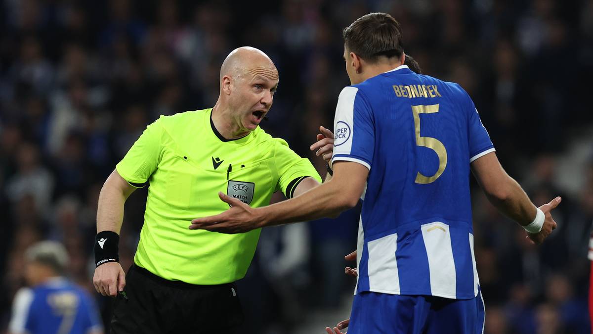 Sędzia piłkarski w neonowoż&oacute;łtej koszulce rozmawia z zawodnikiem w niebieskiej koszulce.