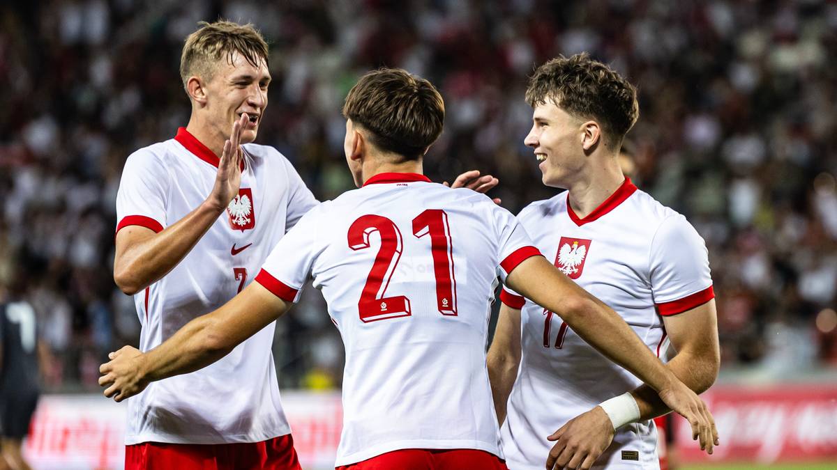 Trzech młodych piłkarzy reprezentacji Polski w białych strojach świętuje po meczu.