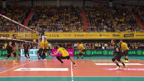 Gracz w ż&oacute;łtej koszulce wykonujący zagrywkę podczas meczu siatk&oacute;wki.