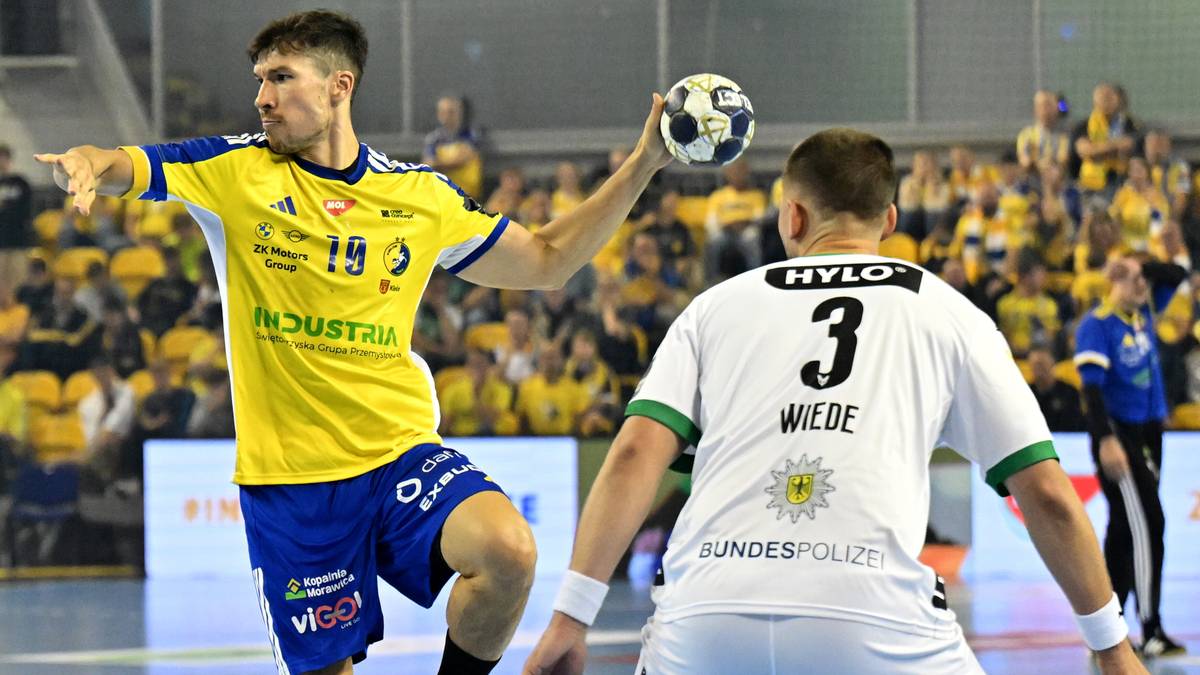 Dwóch graczy w piłce ręcznej podczas meczu. Jeden w żółtej koszulce z numerem 19 i logo "INDUSTRIA" wskazuje palcem w kierunku przeciwnika, drugi w białej koszulce z numerem 3.