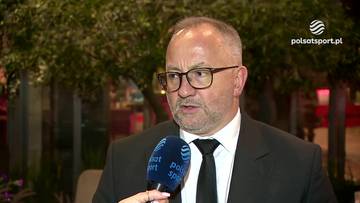 Grzegorz Bachański w okularach, czarnym garniturze i krawacie, udzielający wywiadu z mikrofonem Polsat Sport.