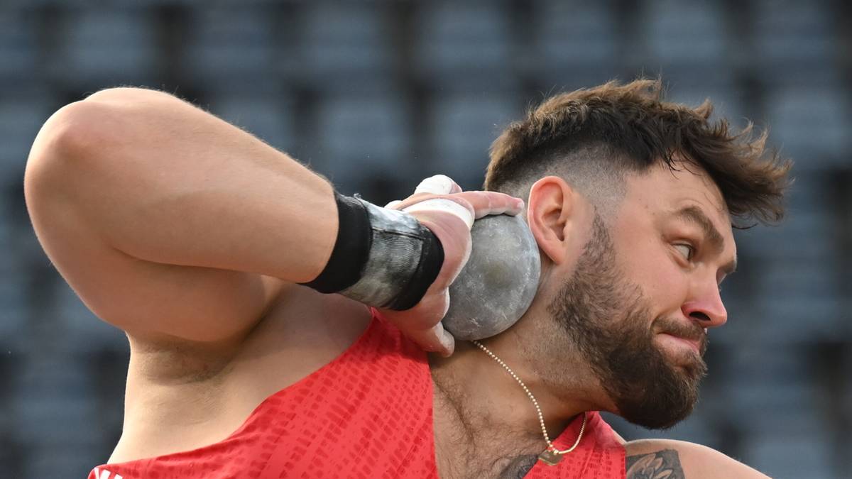 Lekkoatleta w czerwonej koszulce z ochraniaczem na nadgarstku, przygotowuje się do pchnięcia kulą.