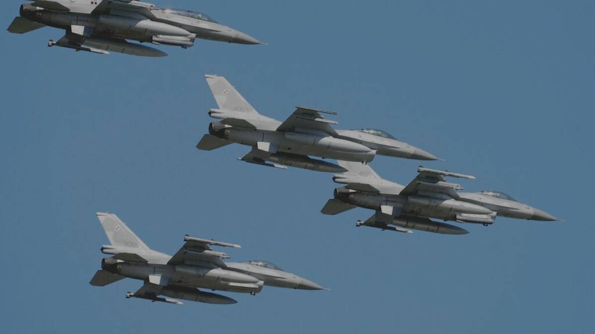 Cztery szare myśliwce F-16 lecące w formacji na tle błękitnego nieba.