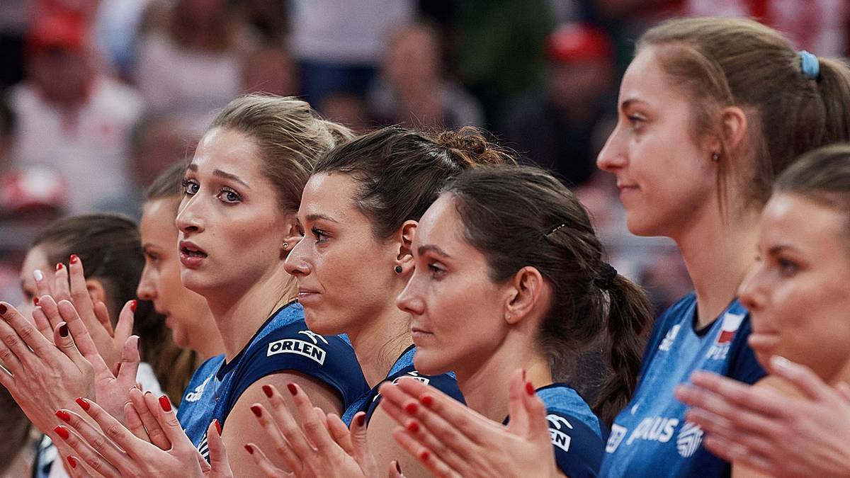 Siatkarki w niebieskich strojach sportowych klaszczą podczas meczu.