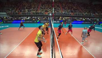 Gracz w ż&oacute;łtej koszulce serwuje piłkę do siatk&oacute;wki, podczas gdy przeciwnicy w czerwonych strojach pr&oacute;bują ją odbić. Mecz odbywa się na pomarańczowym boisku z siatką pośrodku, w tle widownia.