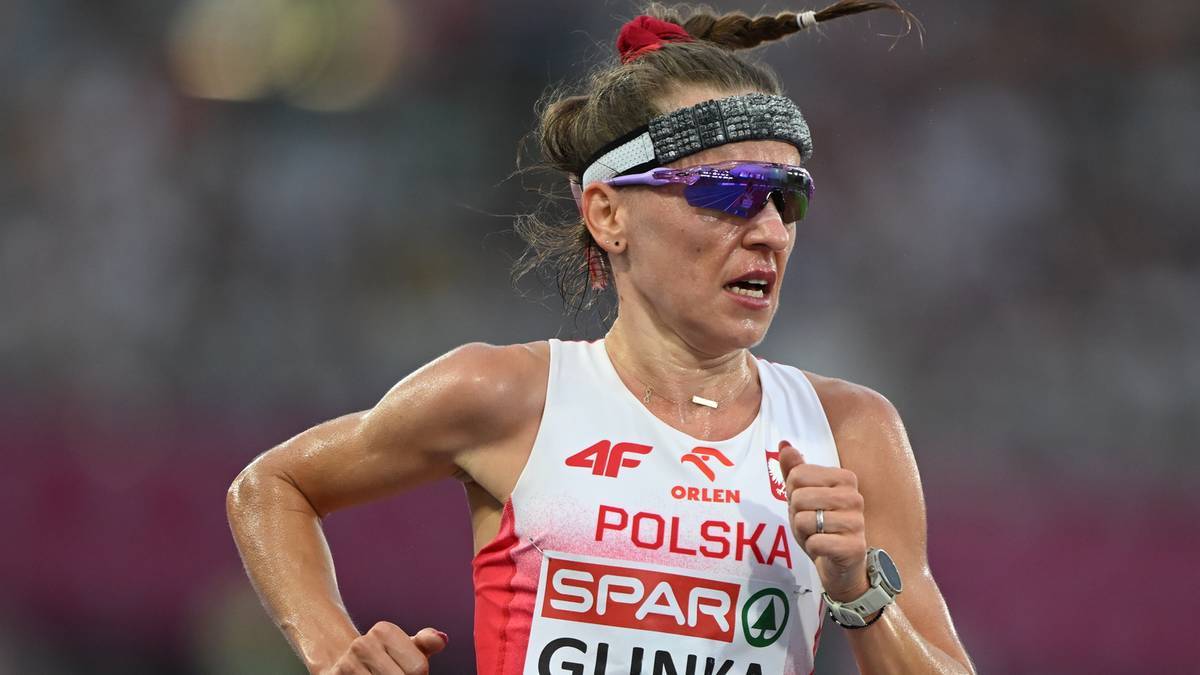 Biegaczka w biało-czerwonym stroju sportowym, okulary przeciwsłoneczne i opaska na głowie.