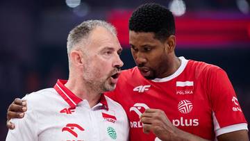 Dwóch mężczyzn w strojach sportowych rozmawia, jeden gestykuluje, drugi słucha.