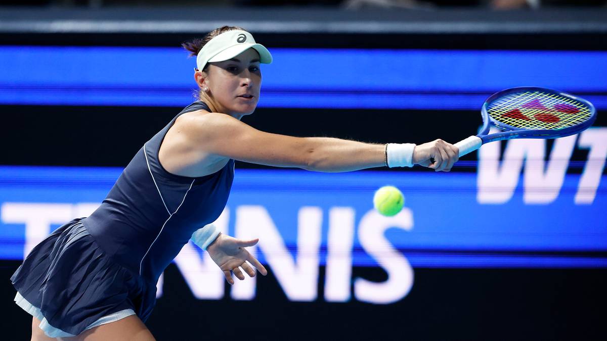 Tenisistka w białej czapce i granatowym stroju odbija piłkę rakietą po lewej stronie.