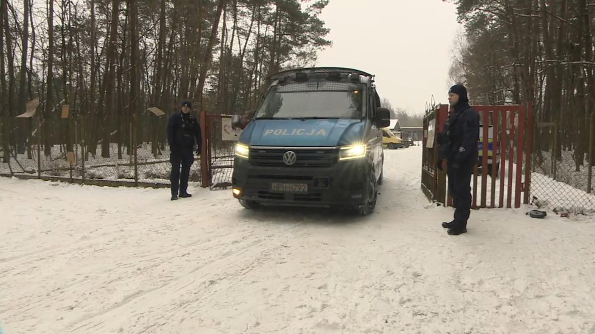 Samoch&oacute;d policyjny "POLICJA" stojący na zaśnieżonej drodze przed bramą schroniska dla zwierząt.