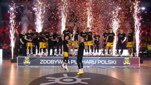 Drużyna koszykarska świętująca zdobycie pucharu Polski, z zawodnikami na podium, fajerwerkami i konfetti w tle.