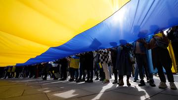 Grupa os&oacute;b trzyma dużą ukraińską flagę, symbol solidarności z Ukrainą.
