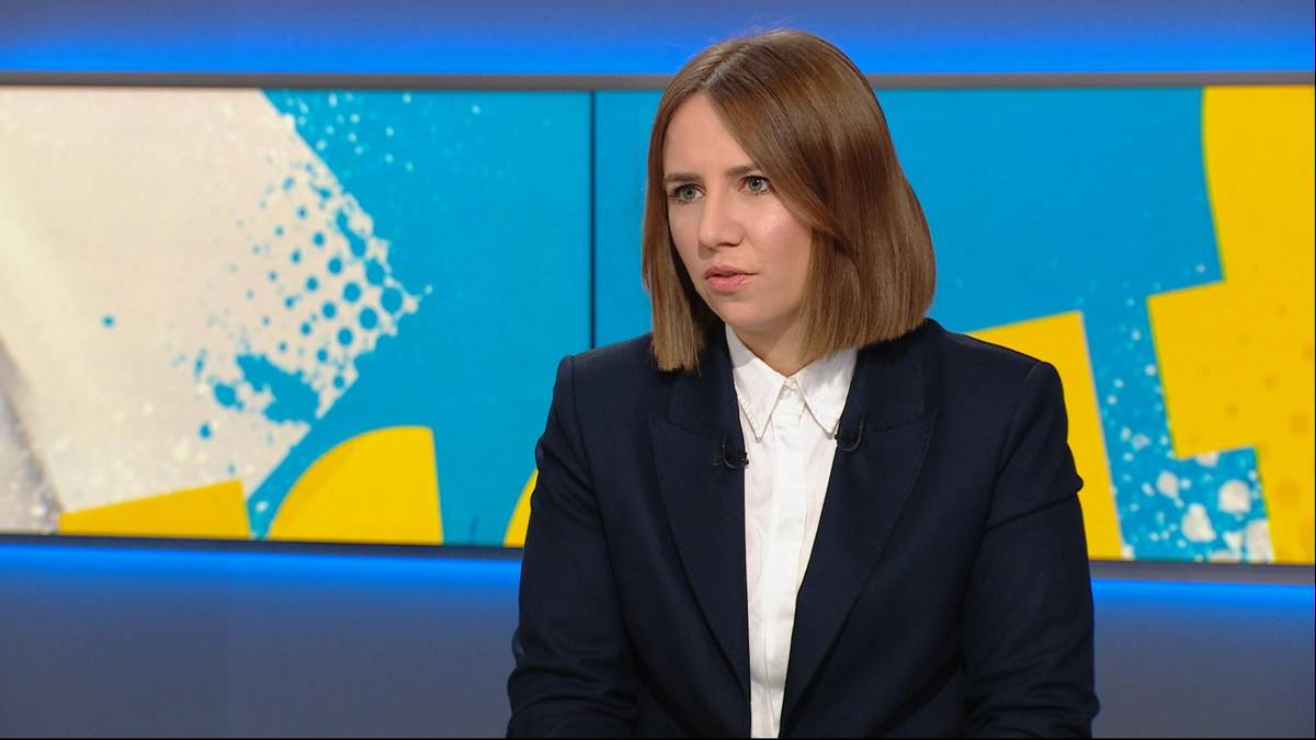 Kobieta w granatowym żakiecie i białej koszuli patrzy w bok.