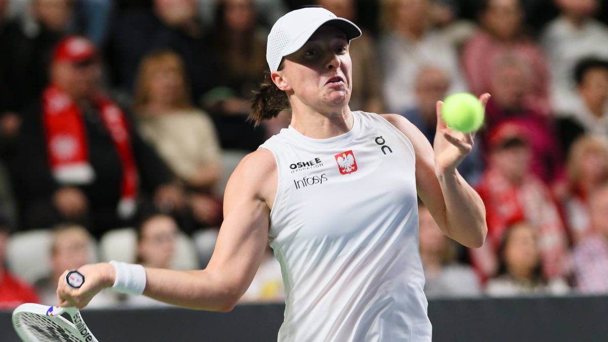 Tenisistka w białej koszulce z godłem Polski i czerwonej spódniczce, z rakietą i piłką w rękach, podczas meczu.