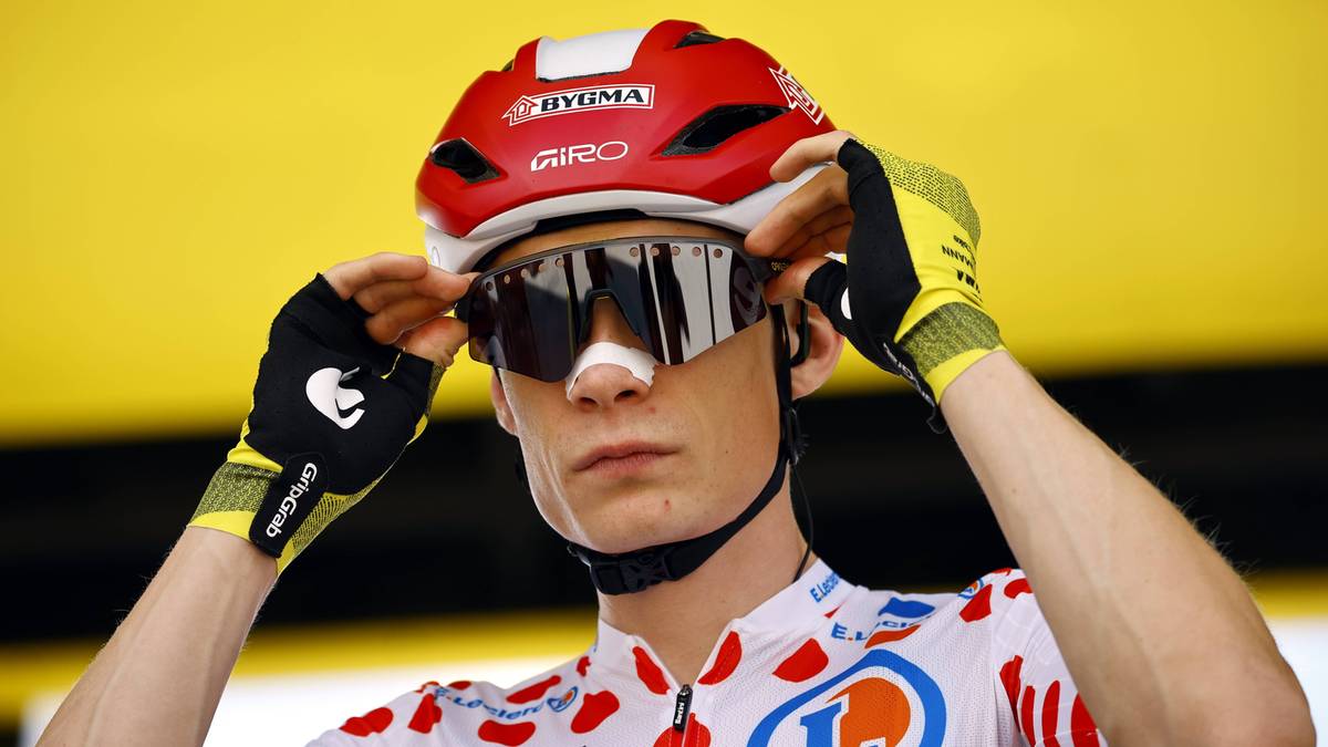 Kolarz w czerwonym kasku i okularach przeciwsłonecznych poprawia rękawiczkę.