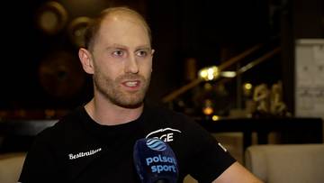 Damian Żurek podczas wywiadu, ubrany w czarną koszulkę z logo.