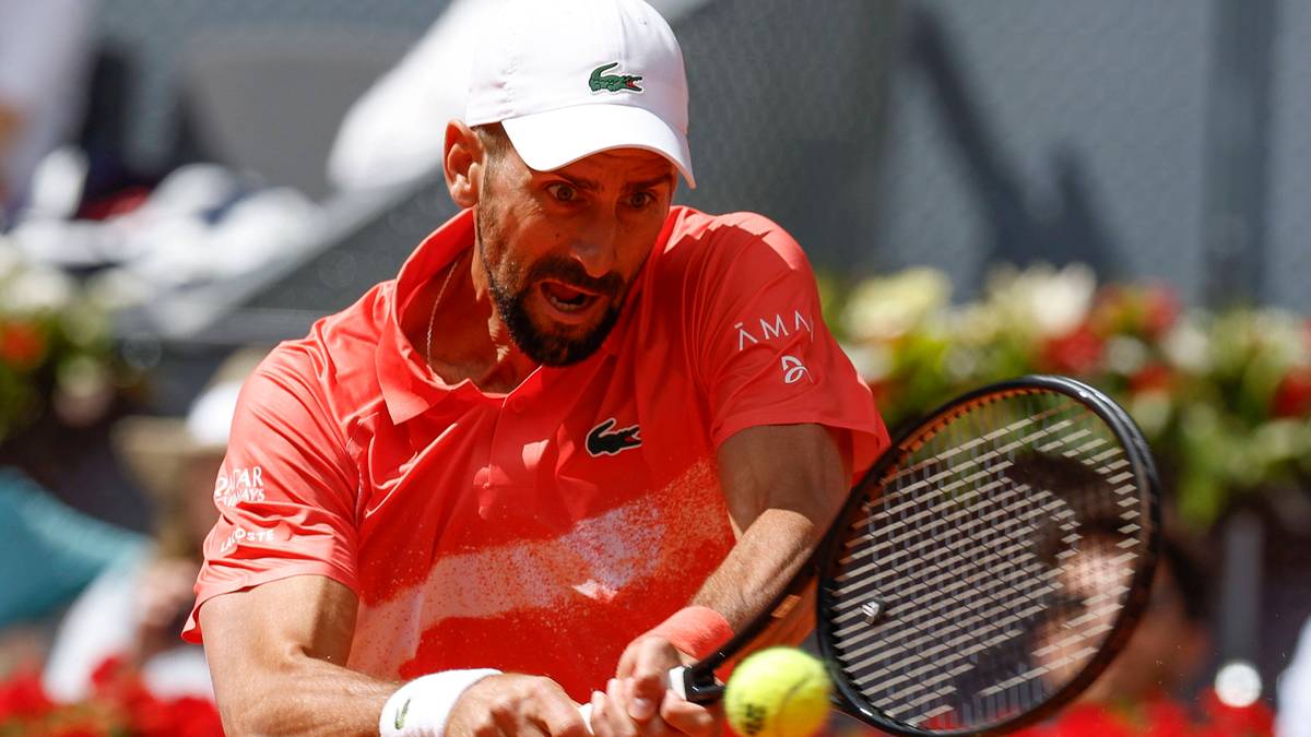 Tenisista w czerwonej koszulce i białej czapce z daszkiem wykonuje serwis.