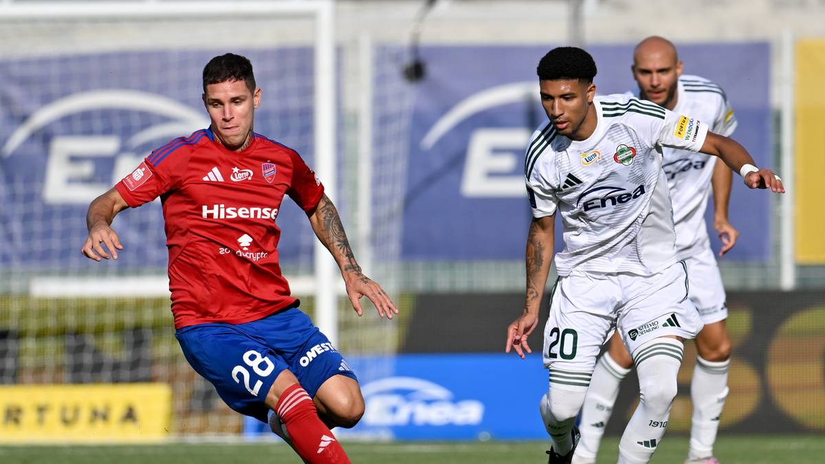 Piłkarze w akcji na boisku, jeden zawodnik w czerwonej koszulce z numerem 28 na plecach, drugi w białej koszulce z numerem 20.