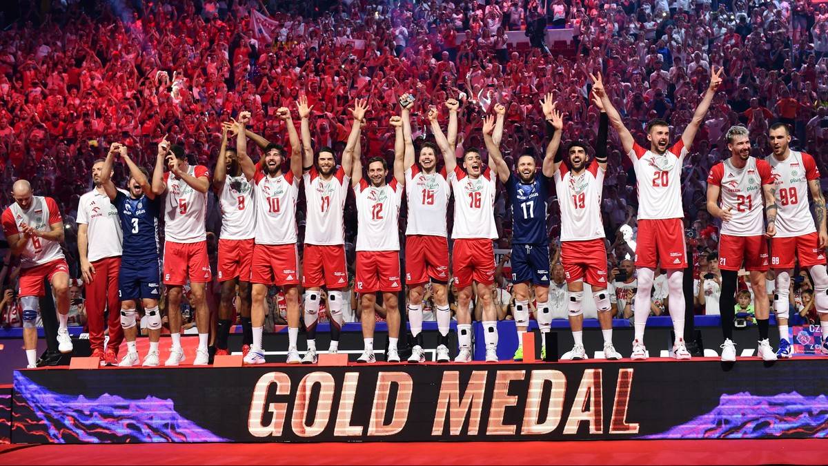 Drużyna siatkarzy w strojach reprezentacyjnych stoi na podium, unosi ręce w geście zwycięstwa. Na pierwszym planie napis "GOLD MEDAL". W tle widać tłum kibiców.