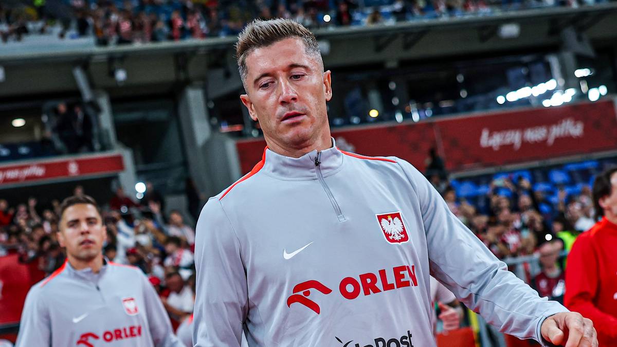 Robert Lewandowski, kapitan reprezentacji Polski w piłce nożnej, w szarym dresie z godłem Polski i logo sponsora.