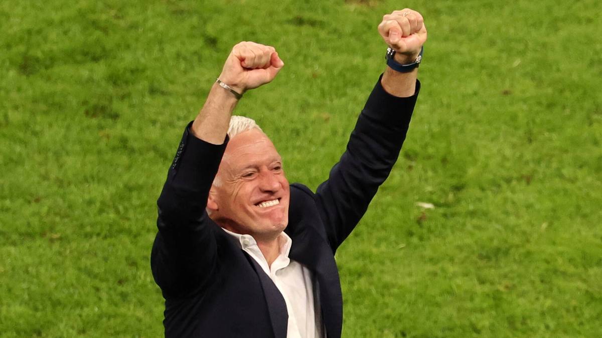 Didier Deschamps, trener reprezentacji Francji, unosi ręce w geście triumfu na tle zielonej murawy.